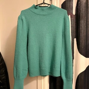 Turkos stickad tröja med puffärm - Mysig turkos stickad tröja med högre ribbad hals och puffiga ärmar. Tröjan har breda muddar vid ärmslut och nederkant, vilket ger en snygg och trendig siluett. Perfekt för att addera färg till din garderob! Använd få gånger 