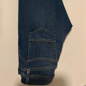 Blå slitna jeans med raka ben - Säljer ett par blå jeans med snygga slitningar och hål på benen. Jeansen har klassisk femficksdesign, raka ben och gul kontrastsöm. Materialet är robust denim som ger en cool och avslappnad vibe. Perfekt för dig som gillar streetstyle och vill ha en edgy look. W30 L32