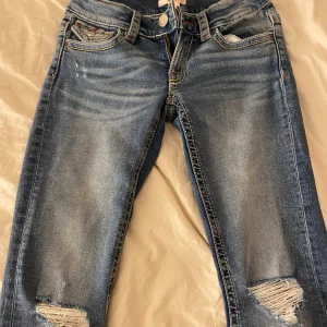 Gina tricot jeans  - Snygga blå jeans med slitna detaljer på knäna och coola röda broderier på bakfickorna. Jeansen är bootcut 