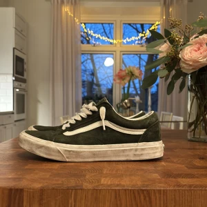 Gröna Vans Old Skool sneakers mocka - Säljer ett par klassiska Vans Old Skool sneakers i mörkgrön mocka med vit sula och vit sidostrip. Skorna har vita snören, rund tå och platt sula. Perfekta för dig som gillar streetstyle och skatevibe.