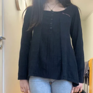 Svart långärmad topp Bondelid XS - Svart långärmad topp från Bondelid i storlek XS. Snyggt knapprad framtill och broderad Bondelid-logga på bröstet. Mjukt material med lätt struktur och broderat hjärta i rött på ryggen. Passar dig som gillar enkel men stilren look.