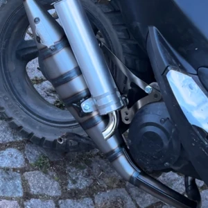 Yasuni R - Bilderna visar en del av en scooter eller moped, främst avgassystemet och bakhjulet. Ingen elektronikprodukt som mobil, surfplatta, dator eller hörlurar syns. Skicket ser bra ut med viss smuts och normalt slitage på plastdetaljer.