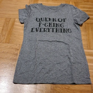 Grå t-shirt med tryck från Patrick XS - Snygg grå t-shirt från Patrick med texten 'Queen of F*cking Everything' i svart på framsidan. Modellen är klassisk med rund hals och korta ärmar. Materialet är en mjuk mix av polyester, bomull och rayon som känns skönt mot huden.