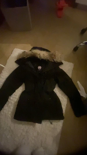 Svart Canada Goose parkas montebello - Säljer en svart fin parkas från Canada Goose montebello med ikonisk patch på ärmen och huva med beige päls. Jackan har dragkedja, knappar och ribbade muddar. Perfekt för kalla vinterdagar och har en snygg, figurnära passform.OPS! säljer inte med pälsen PRIS KAN DISKUTERAS