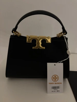 Tory Burch mini Elenor satchel  - Mini elenor satchel liknande Tory Burch svart med guld detaljer. Aldrig använd. Kommer med axelrem. 