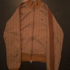 Brun mönstrad ziptröja från Lacoste - Säljer nu denna tröjan från Lacoste då den inte kommer till användning. Storlek S men passar M. Den är endast använd ett fåtal gånger. Finns inga tecken på användning som jag ser. Priset kan diskuteras.