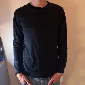 Mörkblå stickad tröja från Bläck - En stilren mörkblå stickad tröja från Bläck i storlek M. Tröjan har rund halsringning och långa ärmar, perfekt för lager-på-lager. Enkel och klassisk design som funkar till många olika outfits.