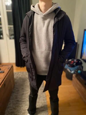 Svart parkajacka från J.Lindeberg - Svart lång parkajacka från J.Lindeberg med stilren design och diskret logotyp på ärmen. Modellen är ca 175 och bär vanligtvis s/m jackan sitter som en smäck. Hör av dig vid minsta funderingar 