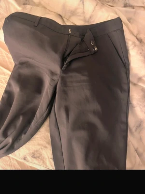 Svarta kostymbyxor med raka ben - Snygga gråa kostymbyxor med klassisk passform och raka ben. Byxorna har hällor för bälte, diskreta sidofickor och en bakficka. Perfekta för en clean och stilren look. Materialet känns slätt och dressat.