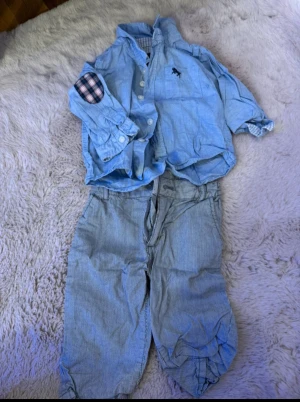 Blå rutig väst  - Snygg blå väst  med rutiga detaljer på insidan och armbågarna. Västen har klassisk krage, knappar framtill och ett broderat logomärke på bröstet. Perfekt för dig som gillar stilrena och coola plagg.