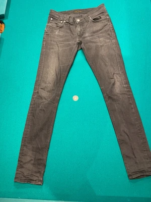 Gråa nudie jeans  - Säljer ett par gråa jeans från Nudie Jeans i storlek W28 L32. Jeansen har klassisk femficksdesign, dragkedja och smal passform. Materialet är mjukt och stretchigt för extra komfort. Perfekta för dig som gillar en slimmad look.