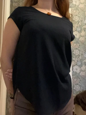 Svart blus med dragkedja bak - Säljer en stilren svart blus från Only med rund halsringning och korta ärmar. Blusen har en snygg dragkedja i ryggen och är lite längre baktill för en chill look. Materialet är mjukt och lätt polyester som faller fint. Perfekt att matcha med jeans eller kjol.