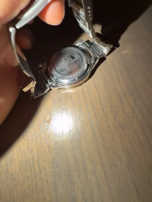 Lotus silverfärgad klocka - En äkta Stilren Lotus herrklocka med silverfärgat metallarmband och svart urtavla. Urtavlan har tydliga indexmarkeringar och en sportig bezel med siffror. Länken är robust och har Lotus-loggan ingraverad på spännet. Perfekt accessoar för dig som gillar klassisk design. Finns även kvitto om man vill ha med 