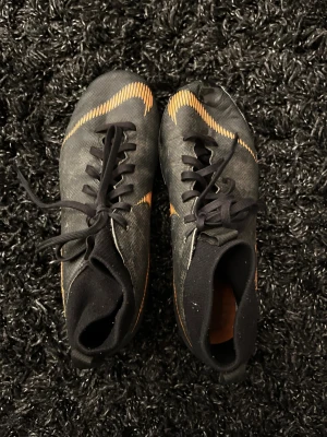 Nike Mercurial svarta fotbollsskor - Säljer mina Nike Mercurial för konstgräs. De är använda och lite slitna, och framtån är skadad men lagad med tejp. Funkar fortfarande bra för träning eller som extra par.  ✔ Bra passform ✔ Lätta och sköna ✔ Perfekt som billigt träningspar  Skick: Använda Pris: 85 kr, Frakt: 25 kr