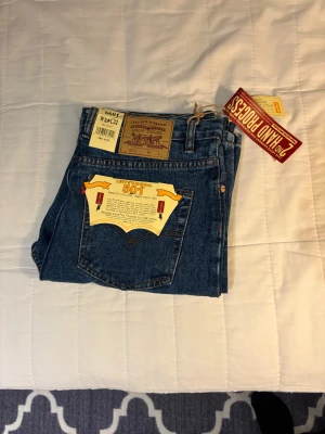 Levi's 501 blå jeans W34 L32 - Klassiska Levi's 501 jeans i blå denim med rak passform och fem fickor. Byxorna har knappgylf, bruna sömmar och Levi's patch bak i midjan. Perfekt för dig som gillar tidlös stil och äkta jeanskänsla.