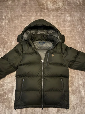Grön  dunjacka från Polo Ralph Lauren - Säljer en grön dunjacka från Polo Ralph Lauren med huva och dragkedja framtill. Jackan har tre fickor med dragkedja och den klassiska Polo-loggan broderad på bröstet. Nypris på jacka ligger runt 5500, där av mitt pris på 2499! Perfekt för kalla dagar och riktigt skön att bära.