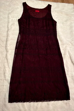 Lila  långklänning från Hugo - Snygg lila långklänning från Hugo med ärmlös design och rund halsringning. Klänningen har tunna lager av mesh med broderade detaljer och små pärlor, vilket ger en lyxig känsla. Perfekt för dig som gillar eleganta och unika plagg med fina detaljer.