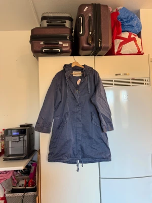 Blå parkajacka Odd Molly Irene - Snygg blå parkajacka från Odd Molly, modell Irene Jacket. Jackan har huva, snörning i midjan och nederkant, praktiska fickor och dragkedja med tryckknappar. Materialet är bomull och jackan har en avslappnad passform som är perfekt för vår och höst. Från märket Odd Molly. Storlek 2 som enligt deras storleksguide motsvarar en M. Mer en L/XL. Armhåla: 60cm. Helt ny med tags/ prislapp fortfarande kvar. 