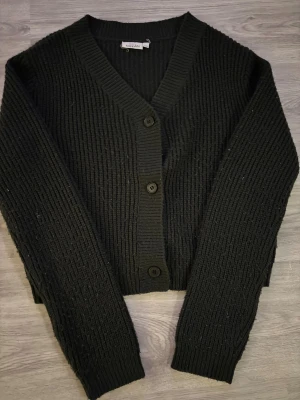 Svart ribbad kofta från KappAhl - Svart, grovstickad kofta från KappAhl med ribbad struktur och v-ringad hals. 