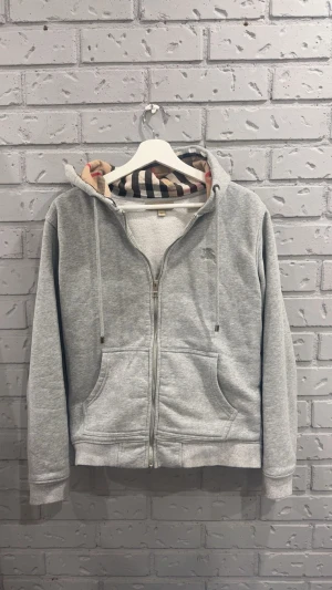 Burberry zip hoodie  - Riktigt snygg grå zip hoodie från Burberry i klassisk stil. Väldigt mjuk och bekväm kvalitet, perfekt både till vardags och träning. Diskret logo och snygga detaljer.