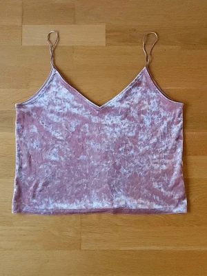 Rosa topp - Ljusrosa linne med v-ringad hals. Toppen är gjord i mjuk sammet som ger en snygg glansig effekt. Perfekt för dig som gillar en chill och trendig look med lite extra lyxkänsla.