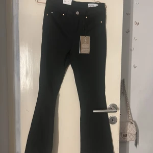 Svarta flared jeans från Vero Moda - Svarta jeans från Vero Moda med flared ben och midwaist. Modellen heter VMFLASH MR FLARED och har klassisk femficksdesign, knapp och dragkedja framtill. Materialet är stretchigt jeans för en bekväm passform. Perfekt för dig som gillar trendiga siluetter.