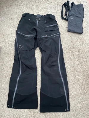 Norrøna Lofoten Gore-Tex Pro Pant storlek Large - Säljer nu mina skidbyxor då jag köpt nya och dessa inte kommer till användning. Söker du ett par schyssta skalbyxor från Norrøna och inte vill betala nypris så är de här ett riktigt bra val!  Har använts i två säsonger och visar tecken på användning (se bilder), men inget som påverkar helhetsintrycket eller funktionen. Jag har försökt fotografera alla ställen där slitage syns.   Storlek: Large Byxans storlek går att justera i midjan.   Nypris idag är: 8999kr  Om du är intresserad och vill ha fle