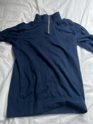Marinblå half zip tröja Jack & Jones - Aldrig använd. Snygg marinblå långärmad tröja från Jack & Jones med half zip-dragkedja i halsen. Tröjan har ribbad nederkant och är tillverkad i mjuk bomull, perfekt för chill dagar. Enkel och stilren design som funkar till jeans eller joggers.