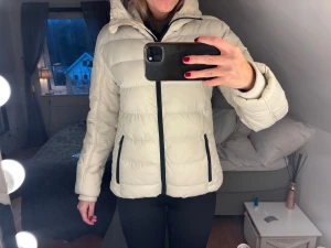 Beige skidjacka från Stimso - Snygg beige dunjacka från Stimson med huva och svarta dragkedjor. Jackan har quiltade detaljer på sidorna och är långärmad. Perfekt för kalla dagar och har en clean, modern look som funkar till många stilar.