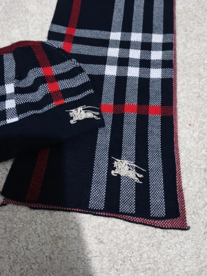 Rutig bomullsväst med broderi - Snygg väst i 100% bomull med klassiskt rutigt mönster i svart, vit och röd. Västen har ett broderat emblem framtill och är mjuk och bekväm. Perfekt för dig som gillar stilrena detaljer och vill sticka ut med en cool look.