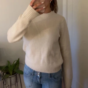 Beige stickad tröja från H&M - Säljer en vit/beige stickad tröja från H&M. Tröjan har en klassisk rund hals och långa ärmar med ribbade muddar.