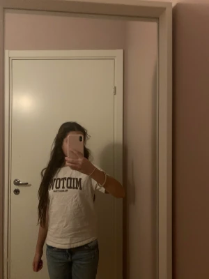 Vit Midtown Manhattan t-shirt från lager 157 - Vit t-shirt med trycket 'MIDTOWN MANHATTAN' i mörkgrått över bröstet. Klassisk rund hals och korta ärmar. T-shirten har en normal passform och är gjord i mjuk bomull, perfekt för en chill och urban look.