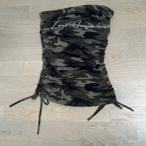 Skitsnygg camo topp - Säljer en camouflagemönstrad tubtopp med snörning i sidorna och strassdetaljer framtill som bildar texten 'Los Angeles'. 