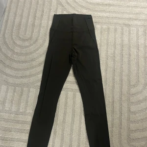 Svarta leggings från Gina Tricot - Svarta, höga leggings från Gina Tricot i storlek S. De har en tight passform och är tillverkade i ett stretchigt syntetmaterial som sitter skönt mot kroppen. Perfekta för dig som gillar en enkel och stilren look med hög midja.