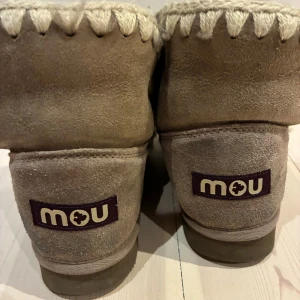 Beige boots från Mou med stickade detaljer - Säljer ett par beige boots från Mou med grova stickade detaljer längs kanterna. Skorna är tillverkade i mjuk mocka och har en rund tå samt platt sula. Insidan är fodrad för extra värme och komfort, perfekt för kyliga dagar. Unik design med tydliga handsydda sömmar.