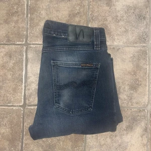 Nudie Jeans - Snygga mörkblå skinny jeans från Nudie Jeans, modell Lean Dean med klassisk femficksdesign och subtila slitningar. Jeansen har en smal passform, svarta detaljer och är tillverkade i ekologisk bomull med lite stretch för extra komfort. Midja 38cm, längd 104cm.  Ifall det inte finns någon bild i annonsen där jag bär plaggen jag säljer så är det för att jag ej kan ha storleken heller passformen, så kolla måtten för storlek och googla på modellnamnet för passform 😉 s4