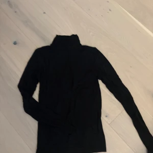 Svart polotröja med lång ärm - Svart polotröja med lång ärm, perfekt för lager-på-lager och chill stil. Mjuk och tunn, med klassisk hög krage som ger en clean look. Snygg att matcha med jeans eller kjol.