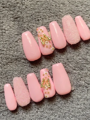 Rosa press-on naglar med fjärilsdekor - Snygga press-on naglar i ljusrosa med glansig finish. Några naglar har 3D-pärlor och små blommor, samt en guldig fjärilsdekor. En nagel per hand har pärlstruktur för extra effekt. Perfekt för dig som vill ha en söt och trendig look.