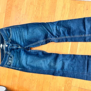 Blå jeans med kontrastsömmar - Snygga blå jeans med vita kontrastsömmar och coola fickor med lock och knapp bak. Modell: Chunky low flare från Gina Young. STORLEK 170! MÅTT: Midja(mätt platt): 39 cm Midjehöjd: 21 cm Innerbenslängd: 80 cm PRIS KAN DISKUTERAS!