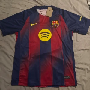 FC Barcelona Lamine Yamal #10 Nike tröja - Säljer en officiell FC Barcelona matchtröja från Nike med Lamine Yamal och nummer 10 på ryggen. Tröjan är kortärmad, har klassiska blå och röda ränder, gula detaljer och klubbmärke på bröstet. Materialet är lätt och andas, perfekt för fotboll eller att representera Barca.