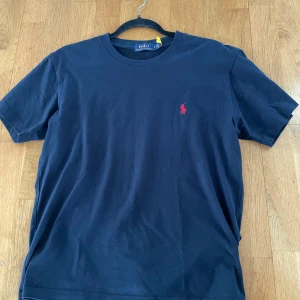 Mörkblå Polo Ralph Lauren T-shirt - Klassisk mörkblå T-shirt från Polo Ralph Lauren i storlek S med loggan broderad i rött. Knappast använd då den inte passade, därav nytt skick. 