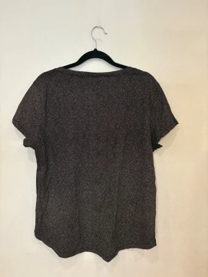 Svart prickig blus från H&M - Svart blus från H&M med små vita prickar över hela tyget. Blusen har rund halsringning och korta ärmar, vilket ger en chill och enkel vibe. Materialet känns lätt och luftigt, perfekt för dig som gillar stilrena mönster och vill ha något som funkar året runt.