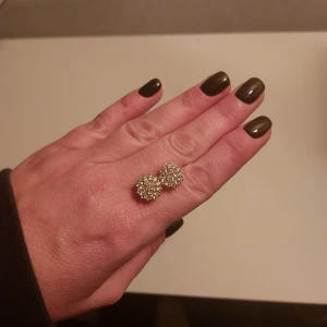 Glittriga guldörhängen - Säljer ett par runda örhängen i guldton med massor av små glittrande stenar. De har en snygg, klassisk design som verkligen drar blickarna till sig. Perfekta om du vill ha något som sticker ut och ger extra bling till din look.