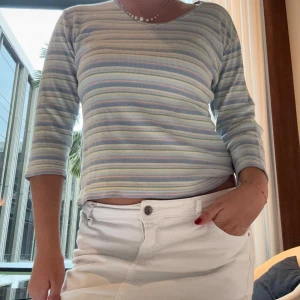 Randig ribbad tröja från Ivy Basics - Pastellrandig ribbad tröja från Ivy Basics med mjuka färger i blått, lila, gult och grönt. Tröjan har trekvartsärm och en rundad halsringning. Perfekt för dig som gillar chill och färgglad stil. Står L men jag har storlek  S 