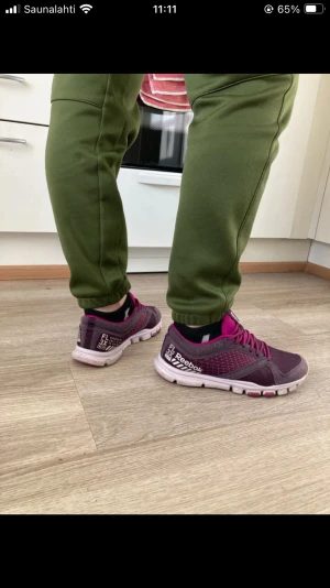 Lila Reebok sneakers med rosa detaljer - Säljer ett par snygga Reebok sneakers i mörklila med rosa mesh och snörning. Skorna har en vit och rosa platt sula med Reebok-logga undertill. Ovandelen är i syntet och mesh för bra ventilation. Perfekta för träning eller chill vardagsstil.