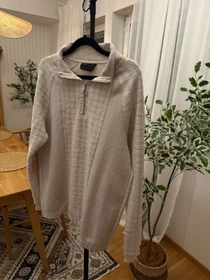 Beige stickad half zip-tröja Asos Design - Snygg beige stickad tröja från Asos Design med half zip och hög krage. Tröjan har långärmade ärmar och en cool textur i materialet som ger en chill vibe. Perfekt för lager-på-lager och passar till jeans eller mjukisbyxor.