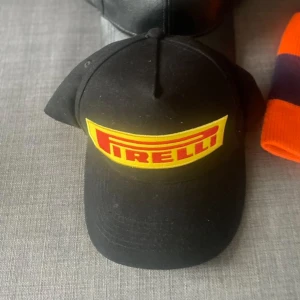 Svart Pirelli keps med gul logga - Svart keps från Pirelli med stor broderad gul patch framtill och röd logotyp. Klassisk böjd skärm och justerbar passform. Tillverkad i 100% bomull för skön känsla och snygg look. Perfekt för dig som gillar motorsport eller vill ha en cool streetstil.