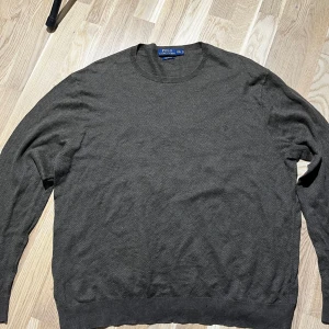 Mörkgrå tröja från Polo Ralph Lauren XXL - Snygg mörkgrå tröja från Polo Ralph Lauren i storlek XXL. Tillverkad i mjuk pima bomull med diskret mönster och rund hals. Långärmad och med klassisk passform, perfekt för dig som gillar stilrena och enkla plagg.