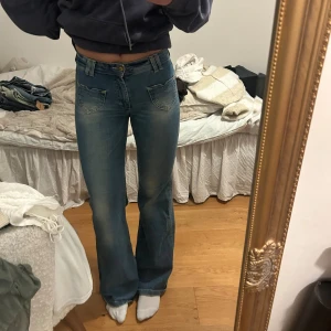 Blå bootcut jeans med låg midja - Säljer ett par blå jeans med snygg bootcut och låg midja. Jeansen har coola fickor med unik form både fram och bak, klassisk knappstängning och bälteshällor. Materialet är klassisk denim och passformen är loose med lite utsvängda ben.