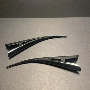 Svarta hårklämmor i plast - Två stilrena svarta hårklämmor i plast med smal och böjd form. Perfekta för att hålla håret på plats när du stylar eller fixar frisyren. Enkel design som passar till alla hårtyper och är lätt att använda. Säljer för använder inte